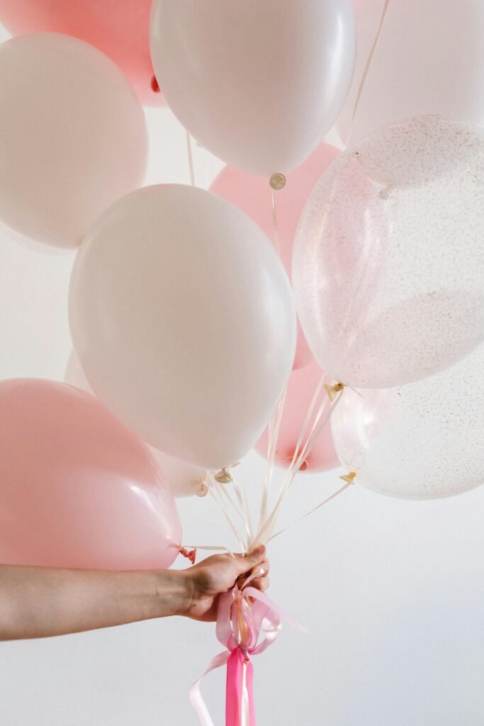 pexels photo 4684169 4684169 A pastel pink and white balloon bouquet held by a hand against a light background, ideal for celebrations.